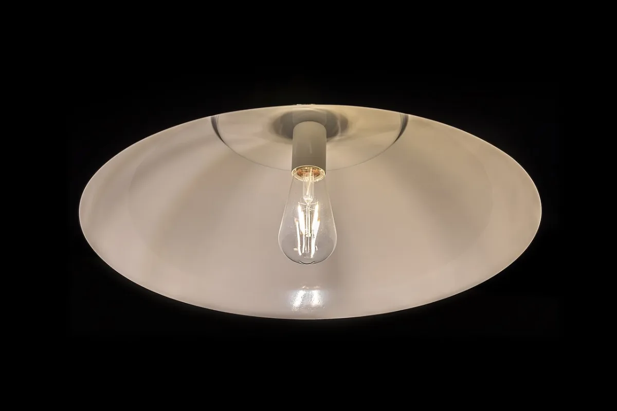Hanglamp met witte kap en brandende gloeilamp met zichtbare filament tegen een zwarte achtergrond